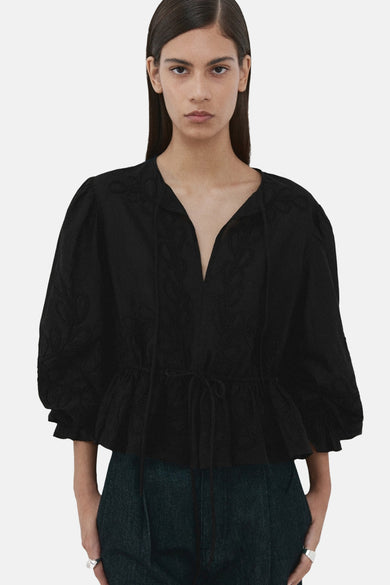 Zwarte blouse met lange mouwen van MANGO, met een diepe V-hals en ruches aan de onderkant.
