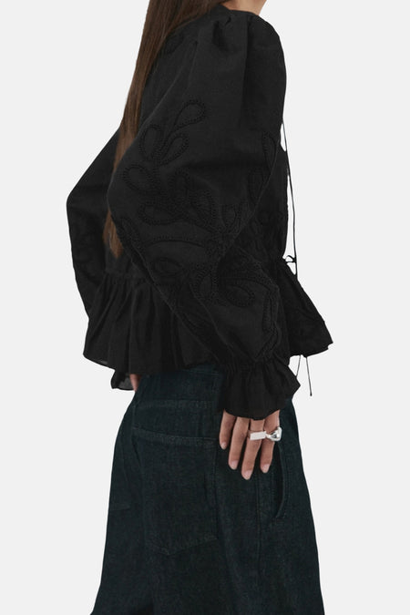 Zwarte blouse met lange mouwen van MANGO, met geborduurde details en een geplooide zoom, gedragen met donkere jeans.
