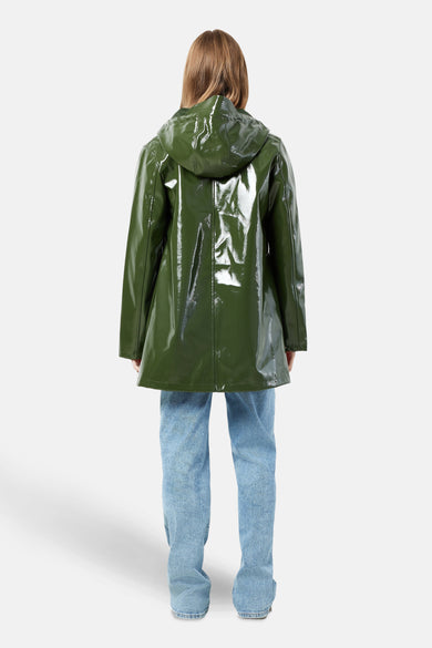 Groene regenjas van DROPLETS, met lange mouwen en capuchon, gecombineerd met een blauwe jeans.
