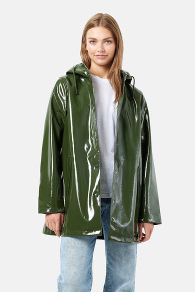Groene regenjas van DROPLETS, met een glanzende textuur en een capuchon, gedragen over een wit T-shirt en een blauwe jeans.
