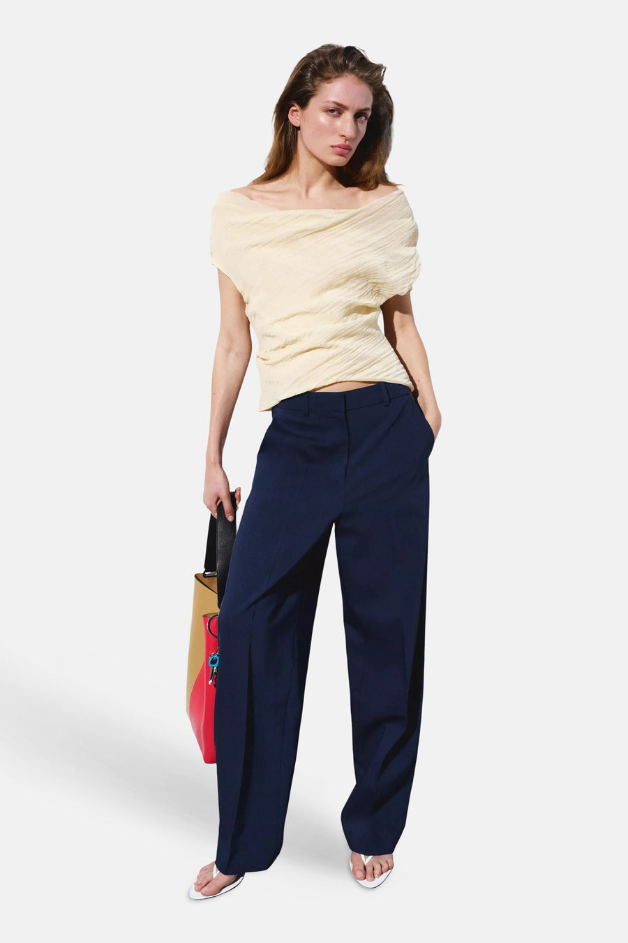 Blauwe kostuumbroek van MANGO met wijde pijpen, gedragen door een model met een crème top en een veelkleurige tas.