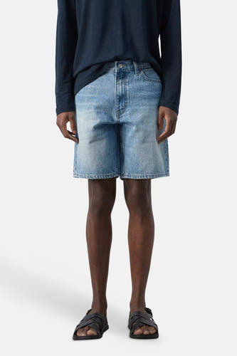 Mid-blauwe denim Bermuda van MANGO met lichte wassing, gecombineerd met een donkerblauw shirt en sandalen.