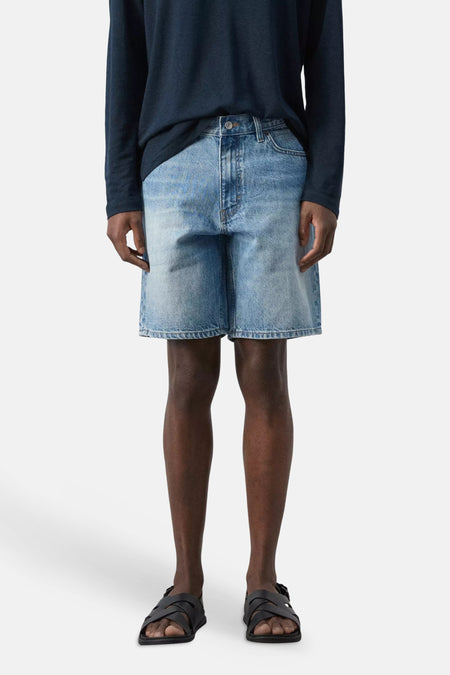 Mid-blauwe denim Bermuda van MANGO met lichte wassing, gecombineerd met een donkerblauw shirt en sandalen.