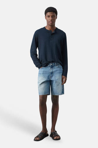 Mid-blauwe denim Bermuda van MANGO, gedragen met een donkerblauw Henley shirt en zwarte sandalen.