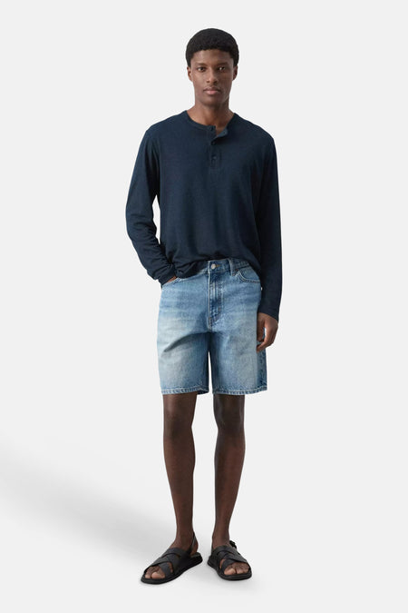 Mid-blauwe denim Bermuda van MANGO, gedragen met een donkerblauw Henley shirt en zwarte sandalen.