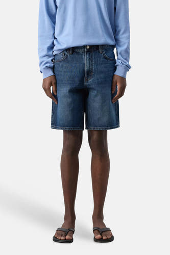 Donkerblauwe denim bermuda van MANGO, gedragen met een lichtblauw shirt en zwarte teenslippers.