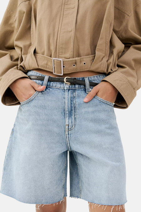 Lichtblauwe denim Bermuda van MANGO, met zwarte riem en rafelige zomen, gedragen met een beige cropped jas.