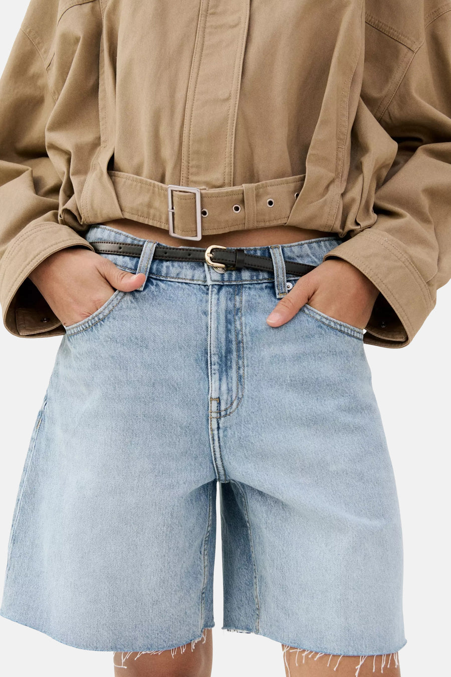 Lichtblauwe denim Bermuda van MANGO, met zwarte riem en rafelige zomen, gedragen met een beige cropped jas.