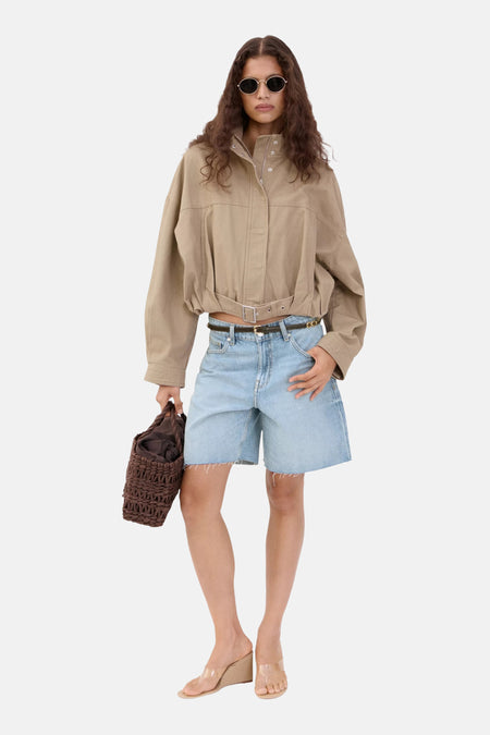 Lichtblauwe spijkerbermuda van MANGO met wijde pijpen en rafelige zoom, gedragen met een beige jasje en heldere sandalen.