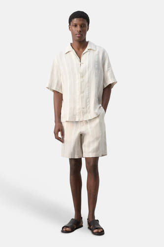 Bermuda beige à rayures de MANGO avec des rayures verticales, porté avec une chemise assortie et des sandales.