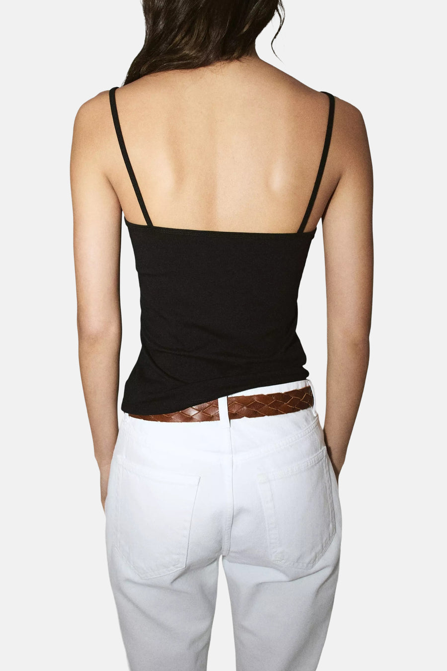 Zwarte spaghettibandjes top van MANGO, achterkant, met slanke bandjes en strakke pasvorm, gedragen met witte broek en bruine riem