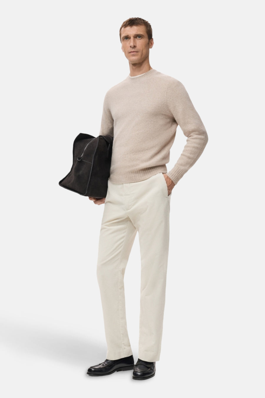 Ecru broek van MANGO, gedragen met een beige trui en zwarte instappers, met een tas in de hand.