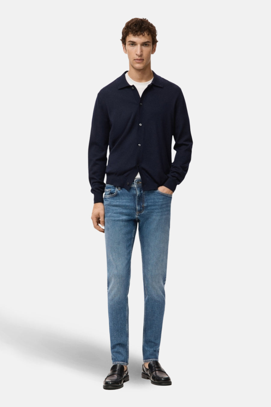 Blauwe slim fit jeans van MANGO, gedragen met een donkerblauw vest, wit T-shirt en zwarte schoenen.