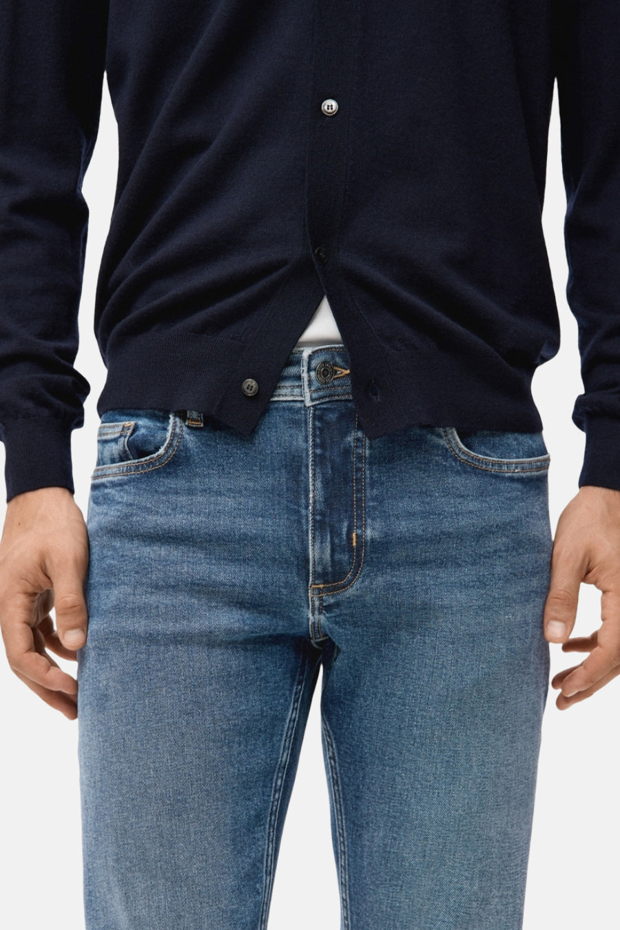 Slim jeans in middenblauw denim van MANGO, met subtiele stiksels en gedragen met een marineblauw vest.
