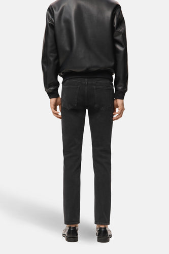 Achterkant van een man in een zwarte leren jas, zwarte jeans en zwarte schoenen.