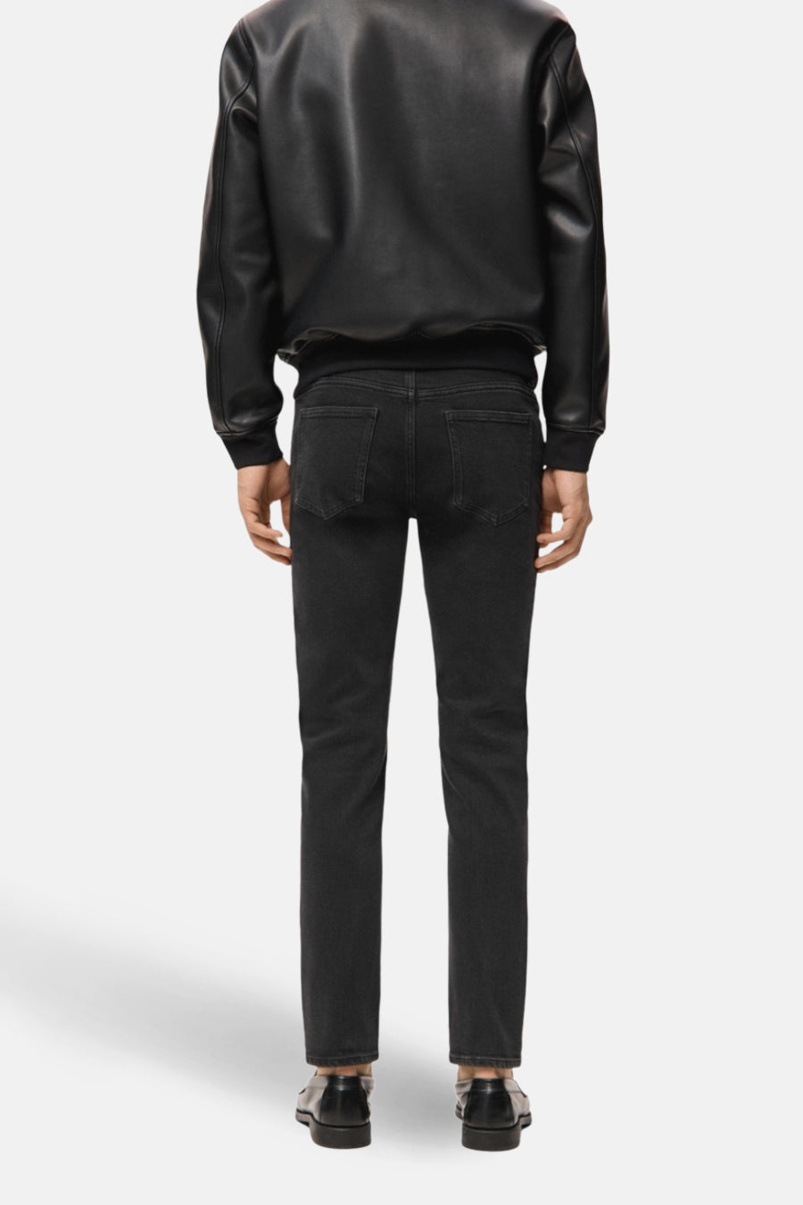 Achterkant van een man in een zwarte leren jas, zwarte jeans en zwarte schoenen.