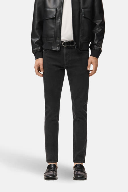 Jean slim gris foncé de MANGO, associé à une ce ce noire, un manteau et des loafers en cuir.