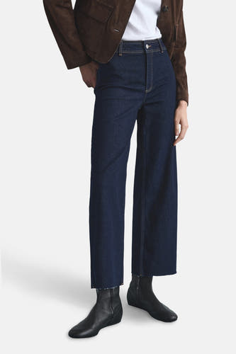 Wijdvallende jeans van donkerblauw denim van MANGO, met een gerafelde zoom en gecombineerd met zwarte laarsjes en een bruin jasje.
