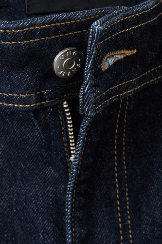 Donkerblauwe wijde jeans van MANGO, met zilverkleurige knoop en ritsdetail, close-up.