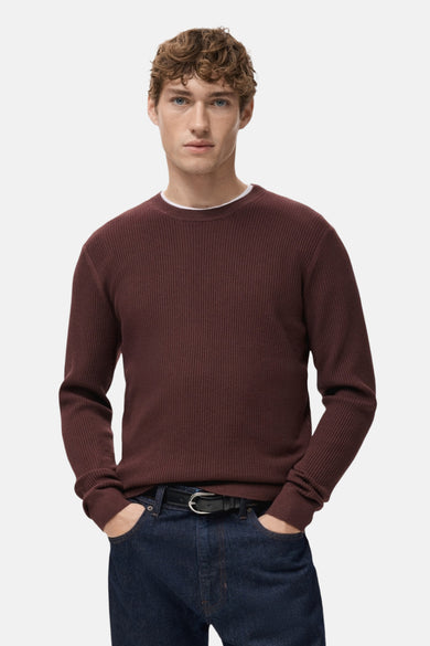 Bordeaux trui met ronde hals van MANGO, met ribgebreide textuur, gedragen over een wit shirt, met donkere jeans.
