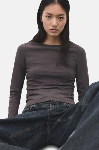 T-shirt gris à manches longues de MANGO, porté avec un jean foncé et un fond uni.