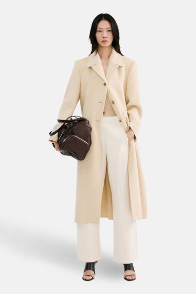 Pantalon de jogging beige de MANGO, combiné avec un long manteau et un sac en cuir marron, sur un mannequin debout.