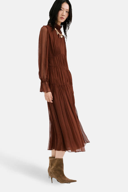 Bruine jurk met lange mouwen van MANGO, met een gelaagde rok en gedragen met suède laarsjes.
