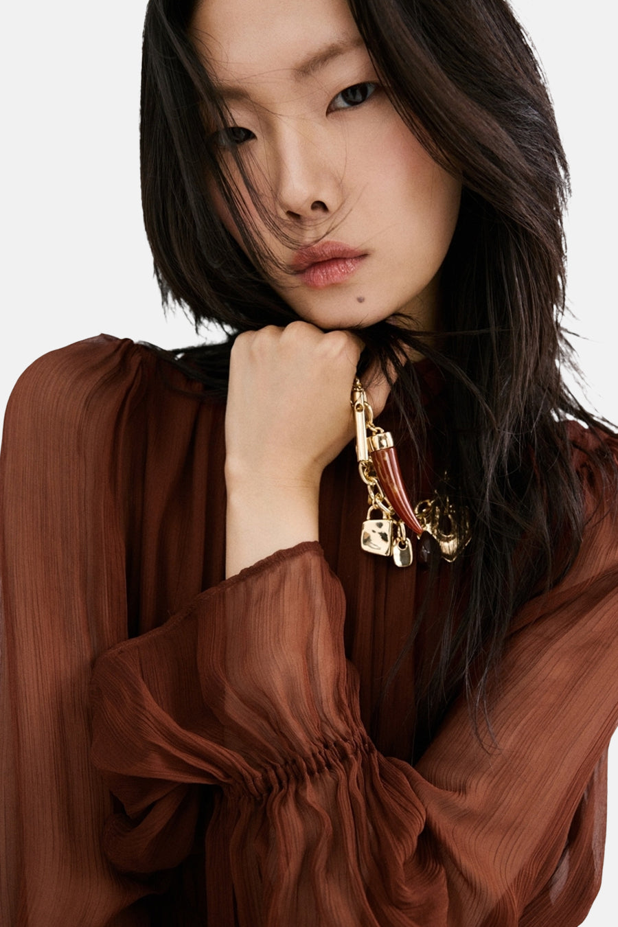 Robe marron à manches longues de MANGO, associée à un collier doré et un tissu transparent.