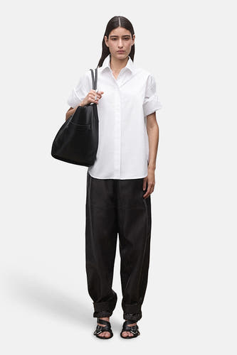 Chemise blanche à manches courtes de MANGO, portée avec un pantalon en cuir noir et des sandales.