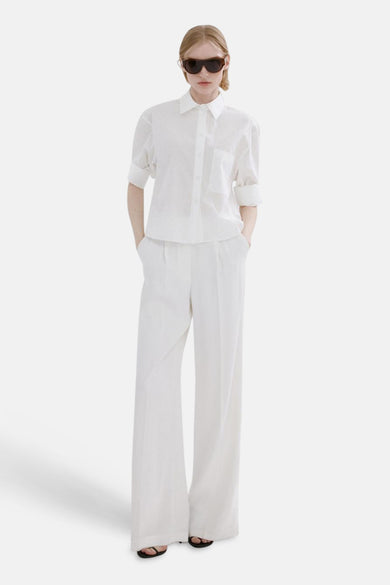 Wit overhemd met lange mouwen van MANGO, gedragen met wijde witte pantalon en zwarte slippers.