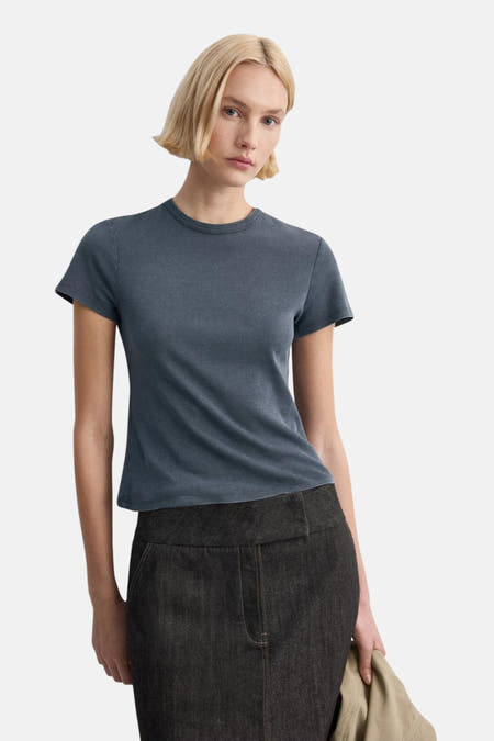 Blauwe top van MANGO, gedragen met een donkere rok, op een witte achtergrond.
