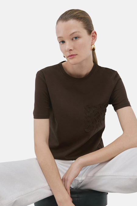 T-shirt marron de MANGO, vu de dos, avec pantalon blanc et boucles d'oreilles dorées.