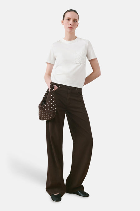 T-shirt blanc à manches courtes de MANGO, avec une poche poitrine en dentelle, combiné avec un pantalon marron et un sac à main.