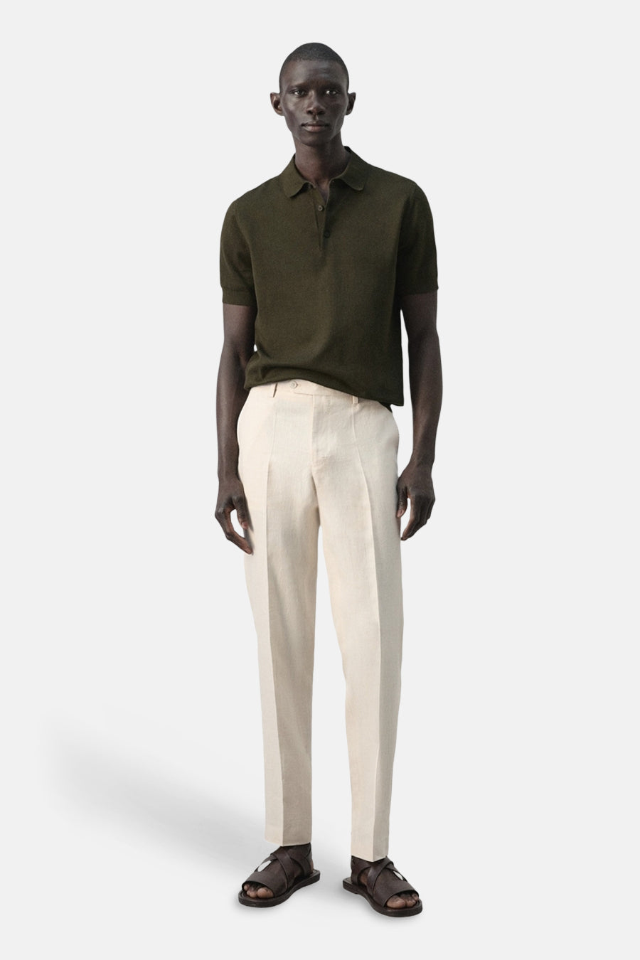 Polo verte de MANGO, portée avec un pantalon en lin de couleur crème et des sandales marron.