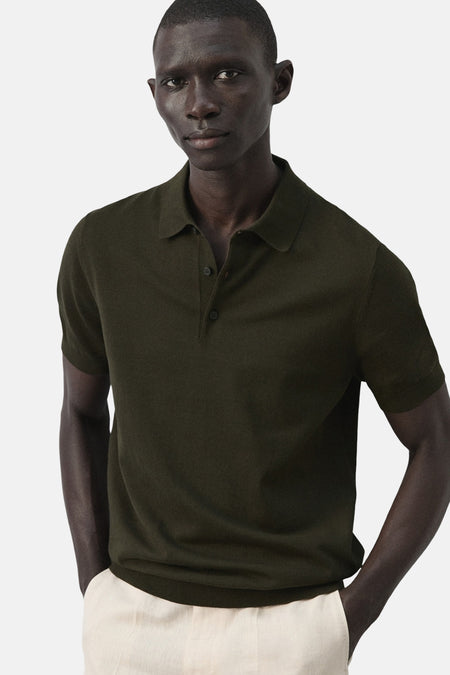 Groene polo van MANGO, met korte mouwen en een knoopsluiting, gedragen met een lichte broek.
