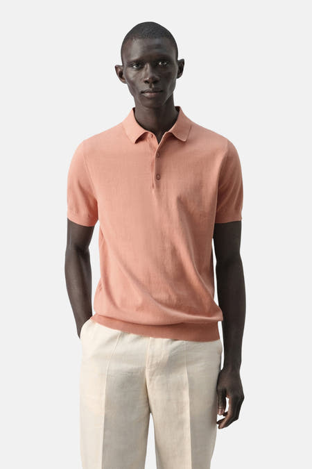 Oranje polo van MANGO, met korte mouwen en een klassieke kraag, gedragen met crèmekleurige broek.
