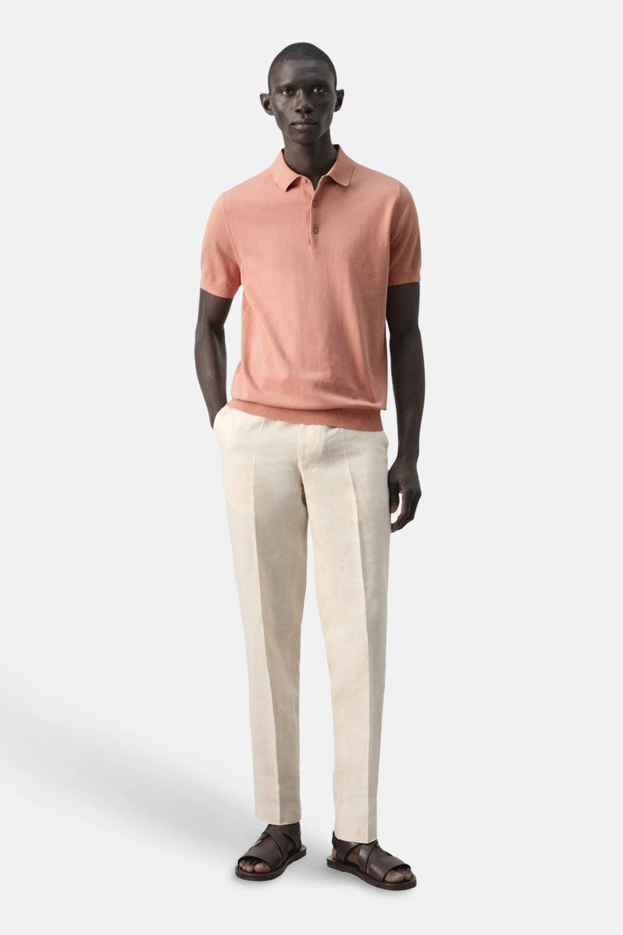 Polo orange de MANGO, à manches courtes, portée avec un pantalon de couleur crème et des sandales marron.
