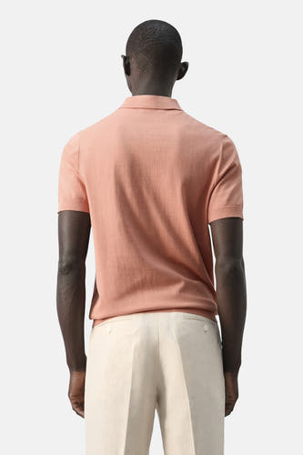 Oranje polo van MANGO, achteraanzicht, gecombineerd met een lichte pantalon.