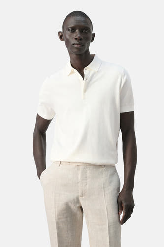 Witte polo van MANGO, gedragen met beige linnen broek, met korte mouwen en knoopsluiting.
