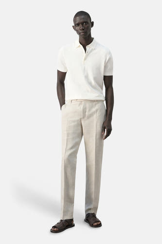 Witte polo van MANGO, met korte mouwen en knoopsluiting, gecombineerd met linnen broek en leren sandalen.
