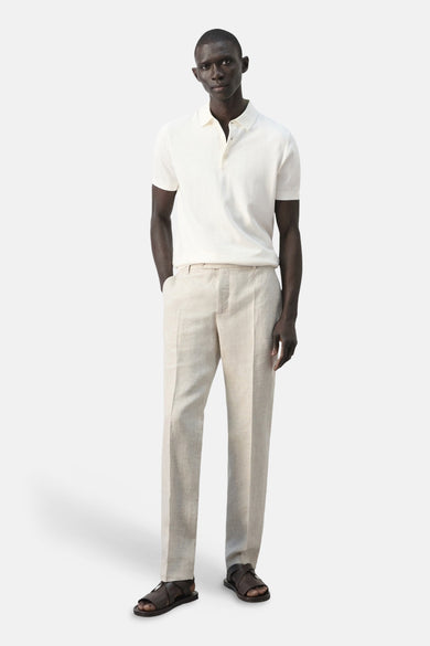 Polo blanche de MANGO, à manches courtes et fermeture boutonnée, combinée avec un pantalon en lin et des sandales en cuir.