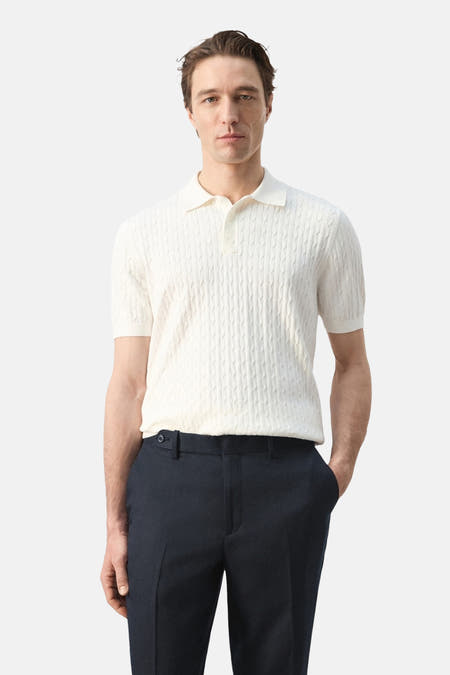 Witte polo van MANGO met kabelstructuur en korte mouwen, gecombineerd met een donkere pantalon.

