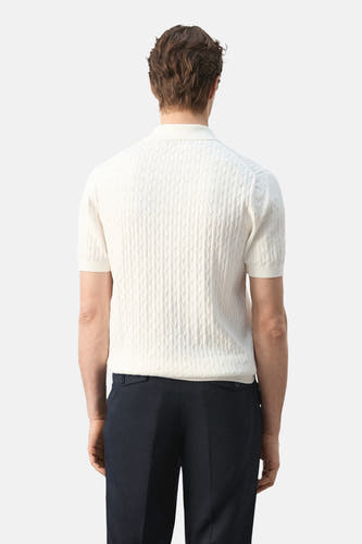 Witte polo van MANGO met korte mouwen en een kabelpatroon op de achterkant, gecombineerd met donkere broek.