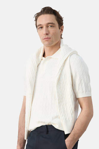 Witte polo van MANGO, met korte mouwen en een kabelpatroon, gedragen met een trui over de schouders.
