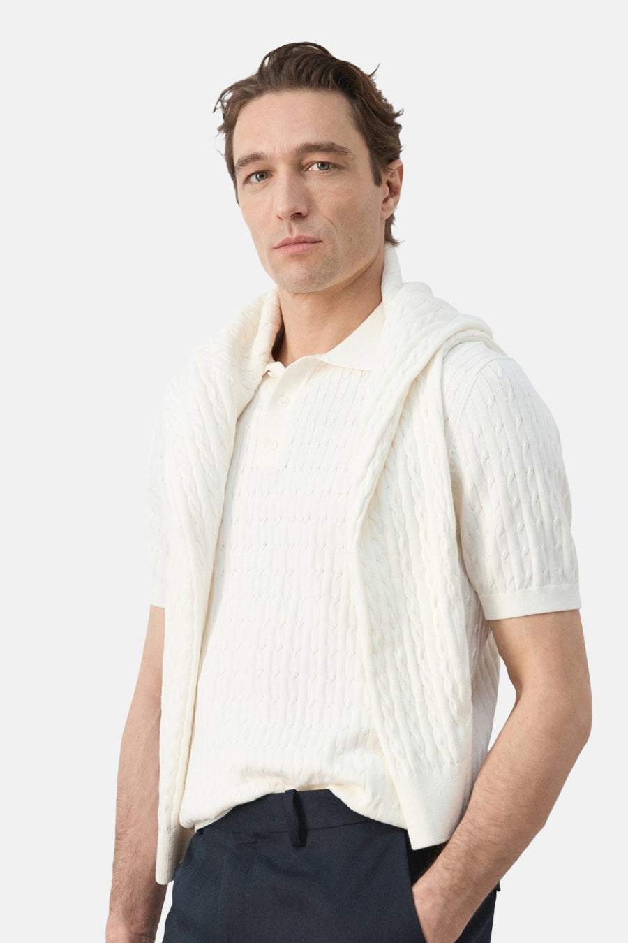 Witte polo van MANGO, met korte mouwen en een kabelpatroon, gedragen met een trui over de schouders.
