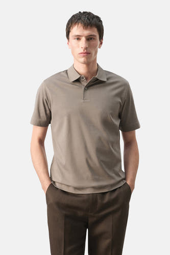 Bruine polo van MANGO, met korte mouwen en een klassieke kraag, gedragen met donkere broek.
