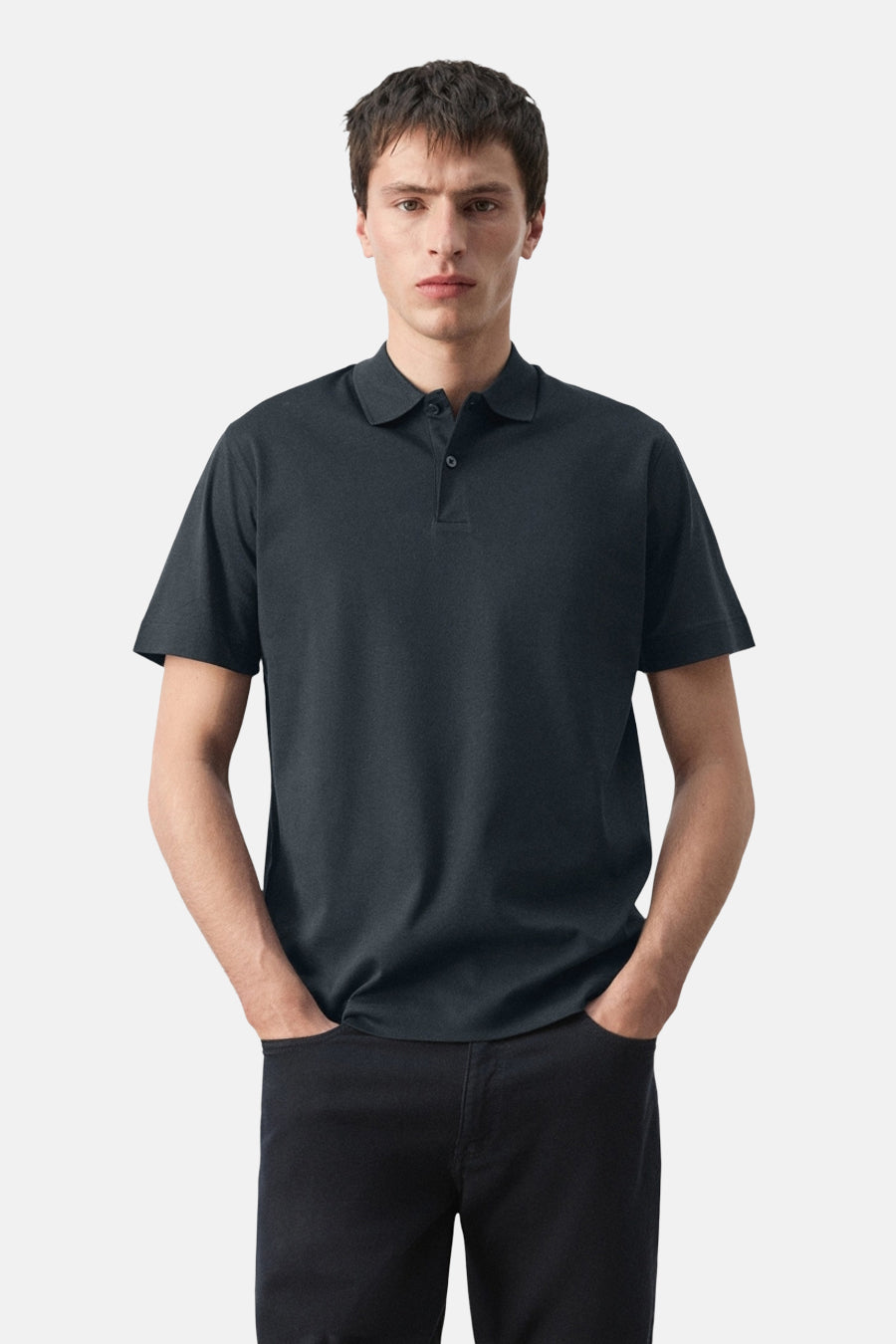 Blauwe polo van MANGO, gedragen met een zwarte broek en met de handen in de zakken.