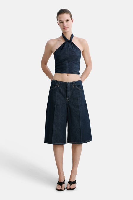 Donkerblauwe denim halternek top van MANGO, gecombineerd met een matchende wijde bermuda en zwarte sandalen.