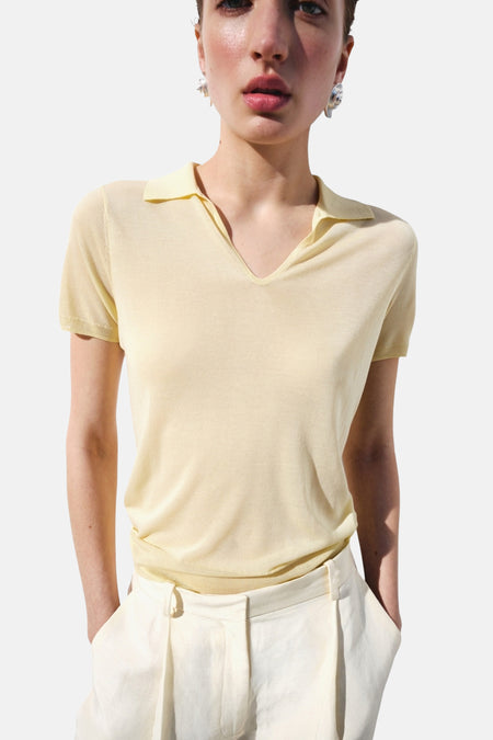 Gele polo met korte mouwen van MANGO, fijn gebreid met V-hals, gedragen op een witte broek.