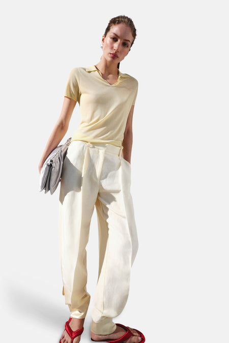 Gele polo met korte mouwen van MANGO met V-hals, gedragen door model met lichte broek en rode sandalen.